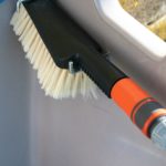 A close up image of the hand brush which is black and orange with softer bristles