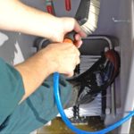 Image shows a man using a handbrush attached to a water pipe to clean his dirty gumboots